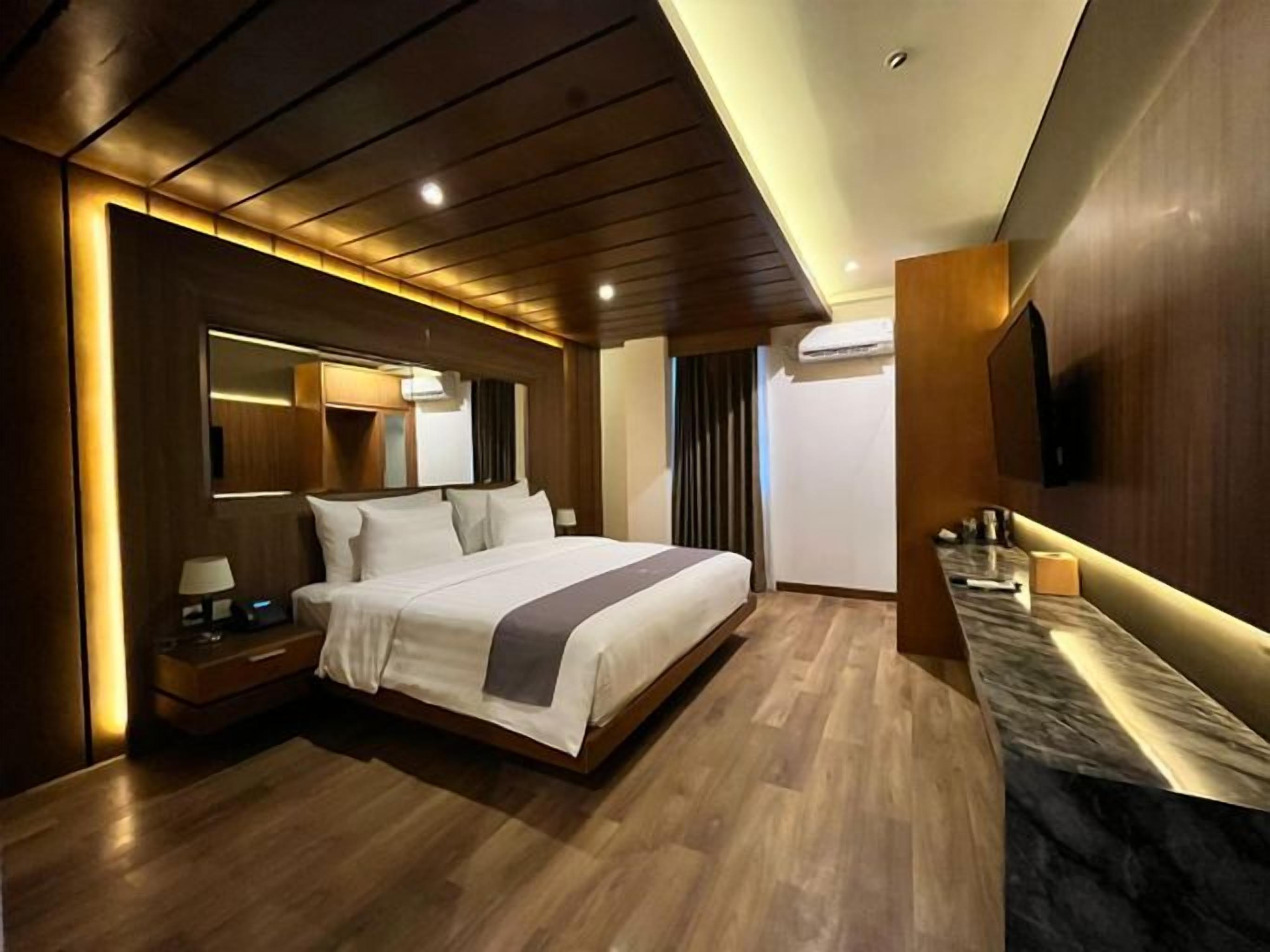 A modern hotel room with a large bed, wooden flooring, a marble countertop, and a wall-mounted TV.