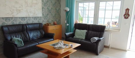 A living room with two black leather sofas, a wooden coffee table, and a large window with curtains.