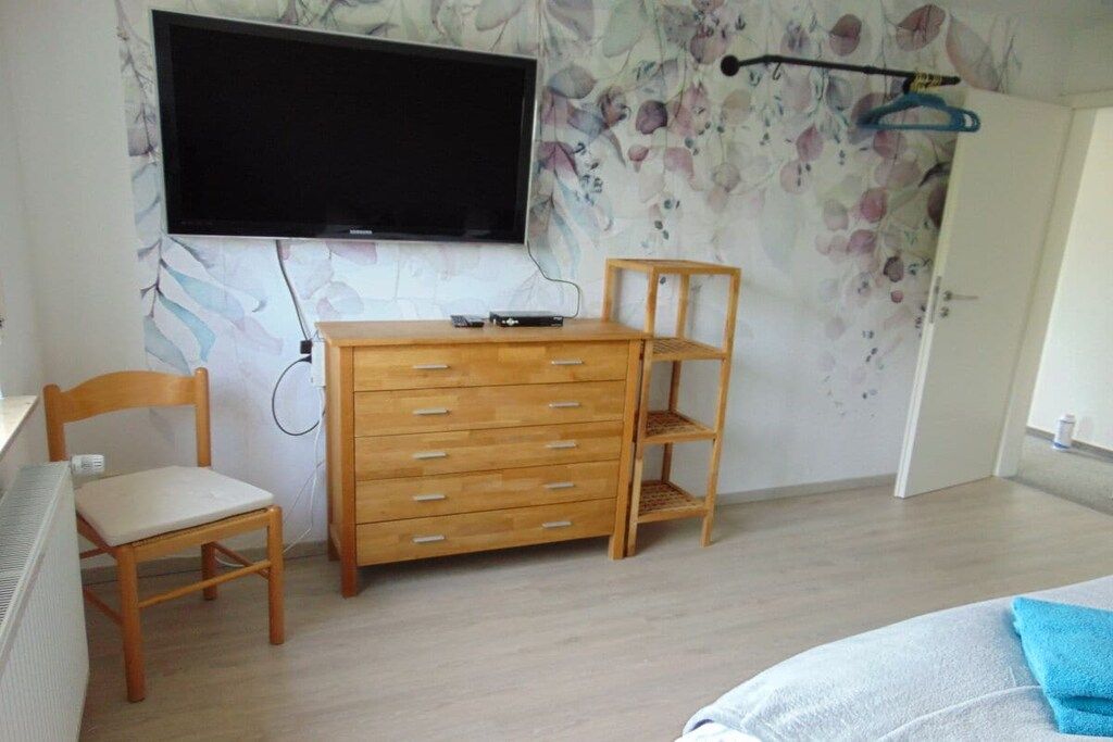 Une pièce comprenant une commode en bois, une chaise, un téléviseur fixé au mur et une porte.