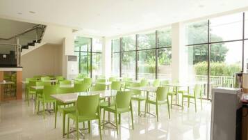 A spacious indoor dining area with green chairs and tables, large windows, and a staircase.