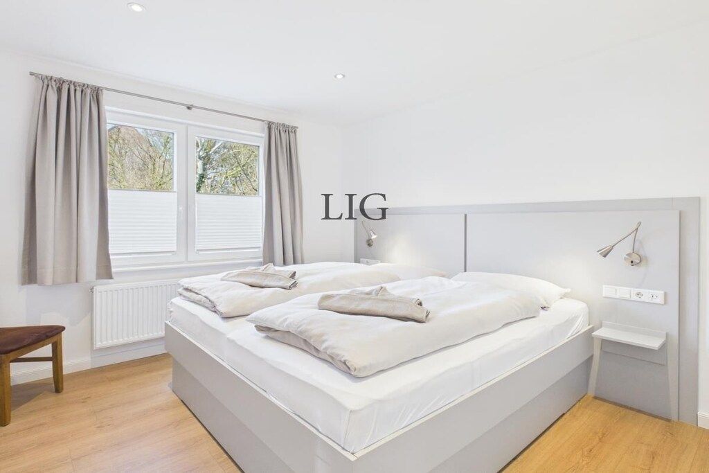 A bedroom with a double bed, a bedside table, a lamp, and a window with curtains.