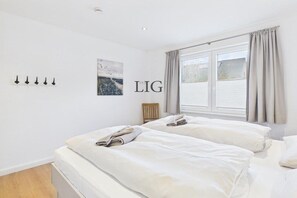 Ein Hotelzimmer mit zwei Betten, einem Fenster mit Vorhängen, einer Wandleuchte und einem Gemälde.