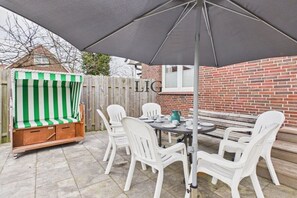 Eine Terrasse im Freien mit Tisch und Stühlen, einer gestreiften Bank und einer Backsteinmauer.