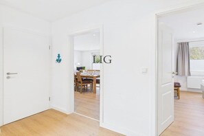 A room with a white door, a dining area with wooden furniture, and a window with curtains. - Holiday apartment Otten 1 (Langeoog)