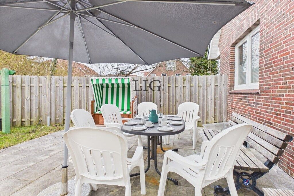 An outdoor patio with a table and chairs, a green and white striped umbrella, and a brick wall.