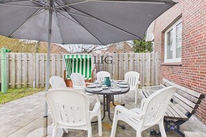 An outdoor patio with a table and chairs, a green and white striped umbrella, and a brick wall. - Holiday apartment Otten 1 (Langeoog)