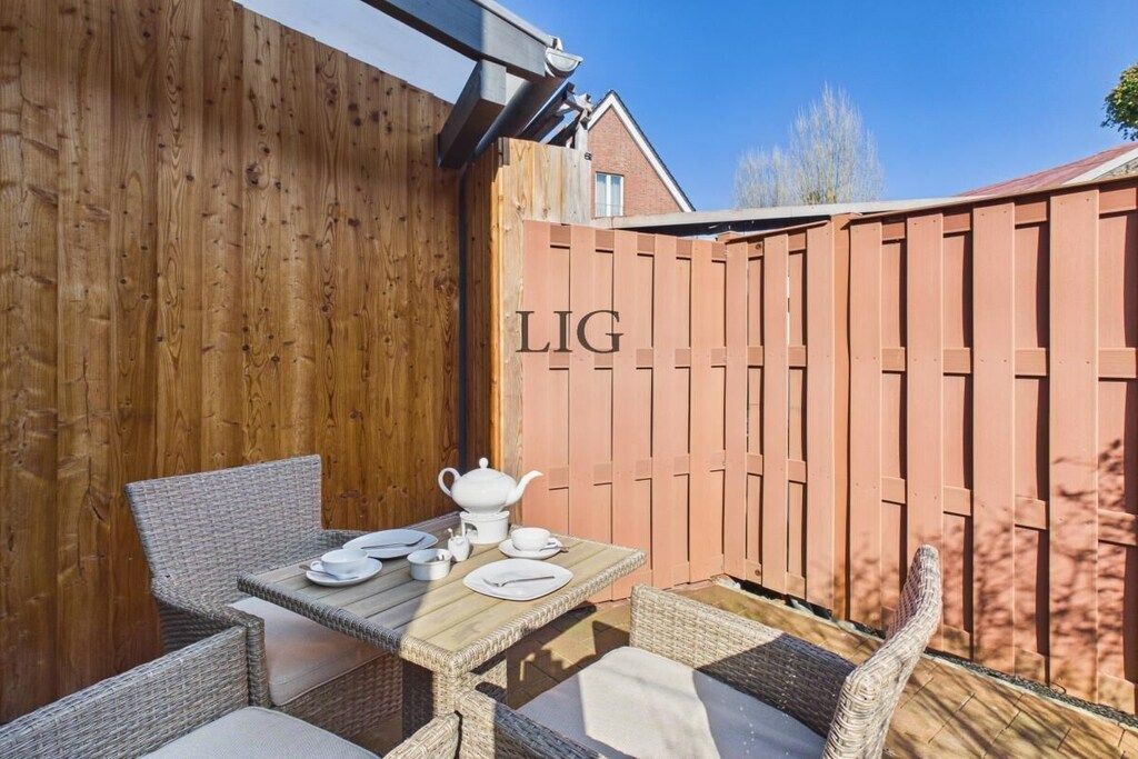 A wooden deck with a table set for tea, wicker chairs, and a wooden fence with 'LIG' written on it.