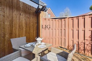 Een houten terras met een gedekte tafel voor thee, rieten stoelen en een houten hek met 'LIG' erop.