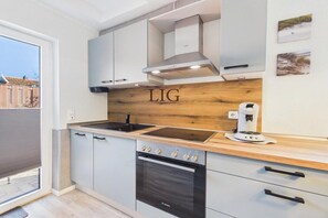 A modern kitchen with a Bosch oven, a coffee machine, and a wooden backsplash. - Holiday apartment Salzwiese (Langeoog)