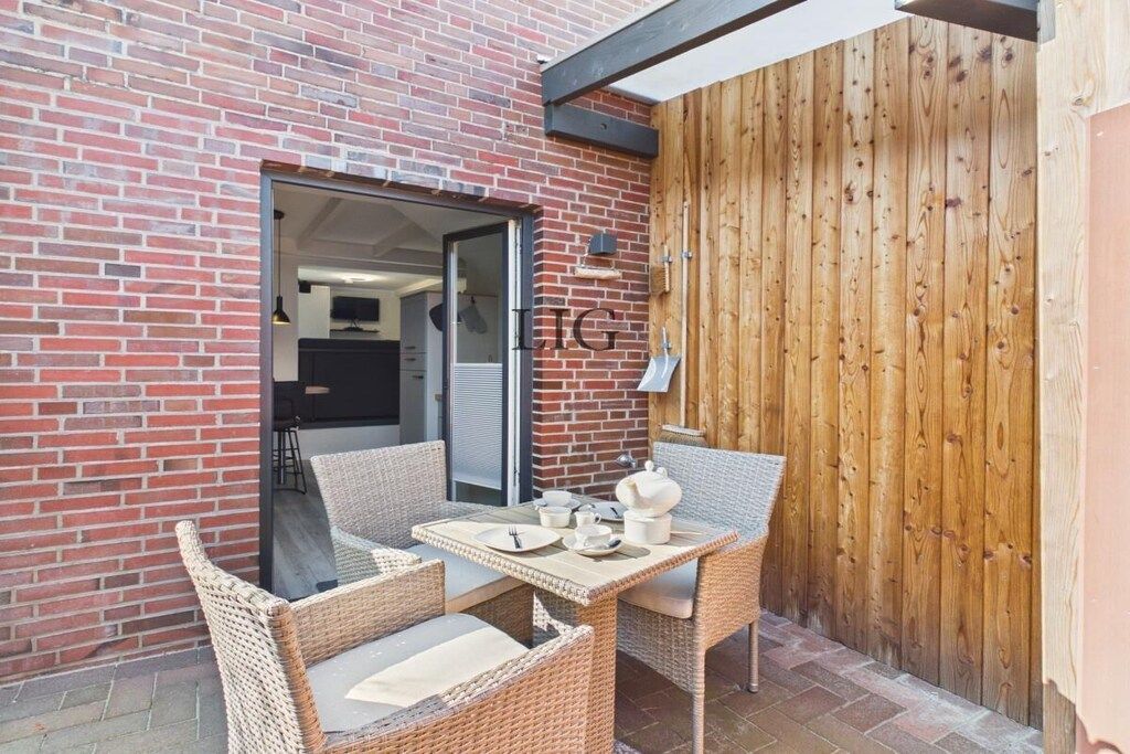 A patio with wicker furniture and a table set for two, a brick wall, and a wooden fence.