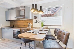 Une cuisine moderne avec un coin repas, comprenant une table en bois, des chaises en cuir noir et des luminaires suspendus.