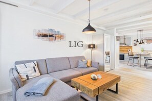 Un salon moderne avec un canapé gris, une table basse en bois et un luminaire suspendu.