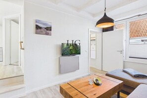 A modern living room with a flat-screen TV, a wooden coffee table, a grey sofa, and a black pendant light. - Holiday apartment Salzwiese (Langeoog)