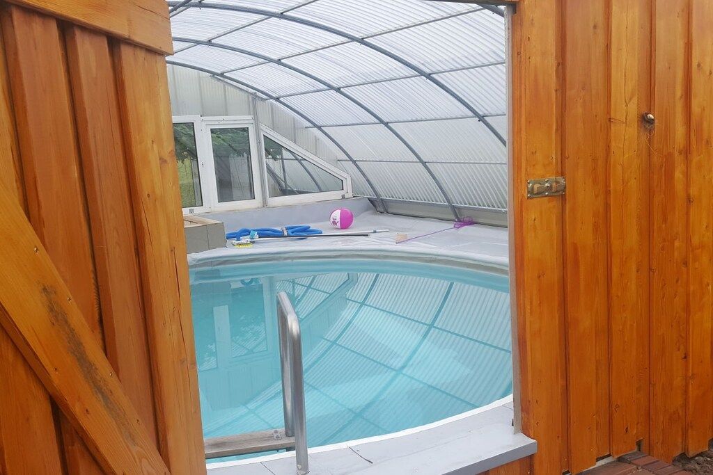 A swimming pool with a wooden deck and a glass enclosure.