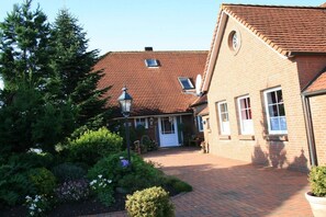Ein Backsteinhaus mit rotem Ziegeldach, einer weißen Tür und einem gepflasterten Innenhof.