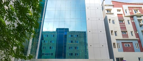 A modern hotel building with a glass facade, a visible entrance, and a sign for 'The Olive Hotel' on the ground floor.