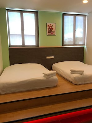 Una habitación con dos camas, cabecero, ventana con vistas e interruptor de luz en la pared.
