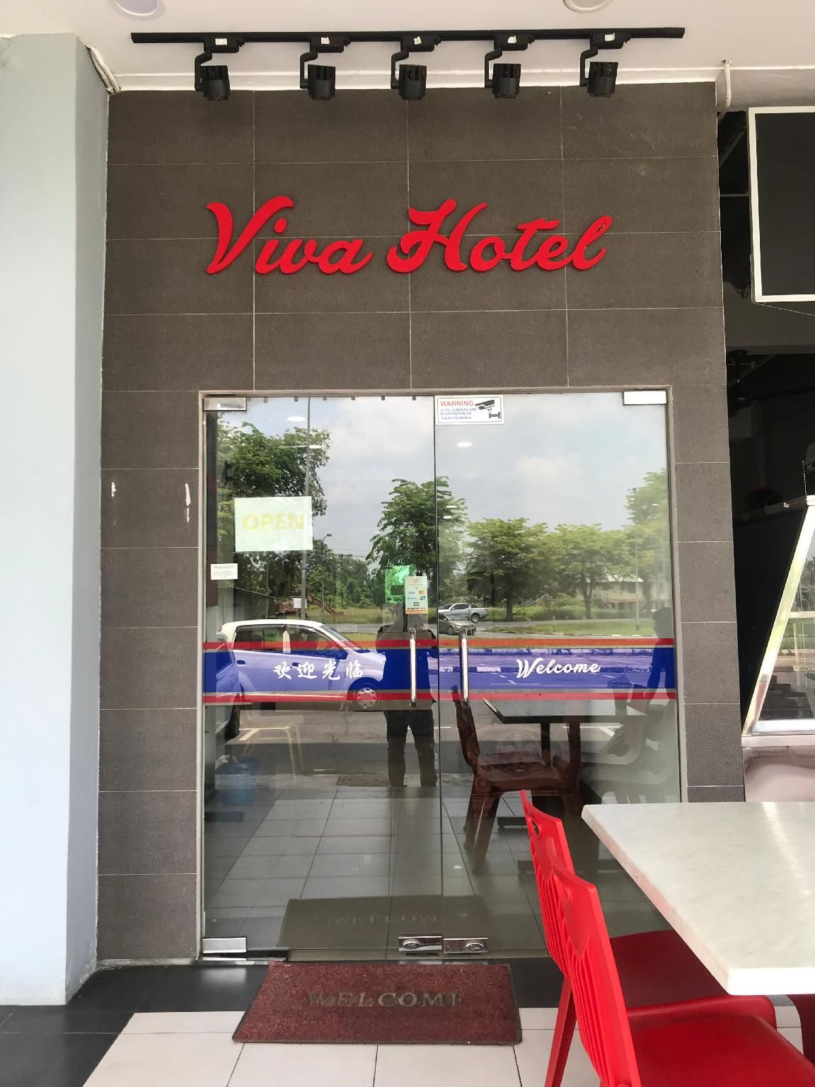 The entrance to Viva Hotel with a glass door, a welcome mat, and a red chair outside.