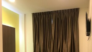 A hotel room with a bed, a small bedside table, a wall-mounted TV, and a curtain. - Viva Hotel SRI Aman (Sri Aman)