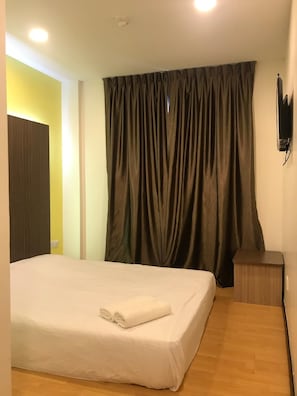 Una habitación de hotel con una cama, una mesita de noche, un televisor montado en la pared y una cortina.