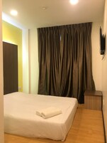 Quarto de hotel com cama, mesa de cabeceira, televisão na parede e cortina.