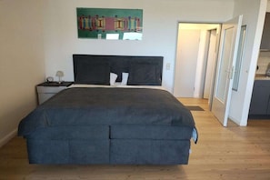 A bedroom with a bed, a nightstand, a wall-mounted artwork, and a door leading to another room. - Holiday apartment with 1 bedroom (Cuxhaven-Döse)