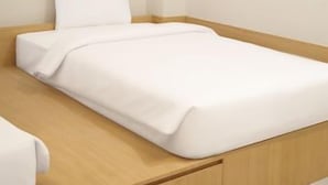 Uma cama de solteiro com cabeceira de madeira, colchão branco e travesseiro branco.
