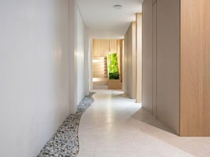Ein moderner Flur mit einem mit Kies belegten Weg, Holzboden und Blick auf eine Treppe, die zu einem Raum mit grüner Wand führt.