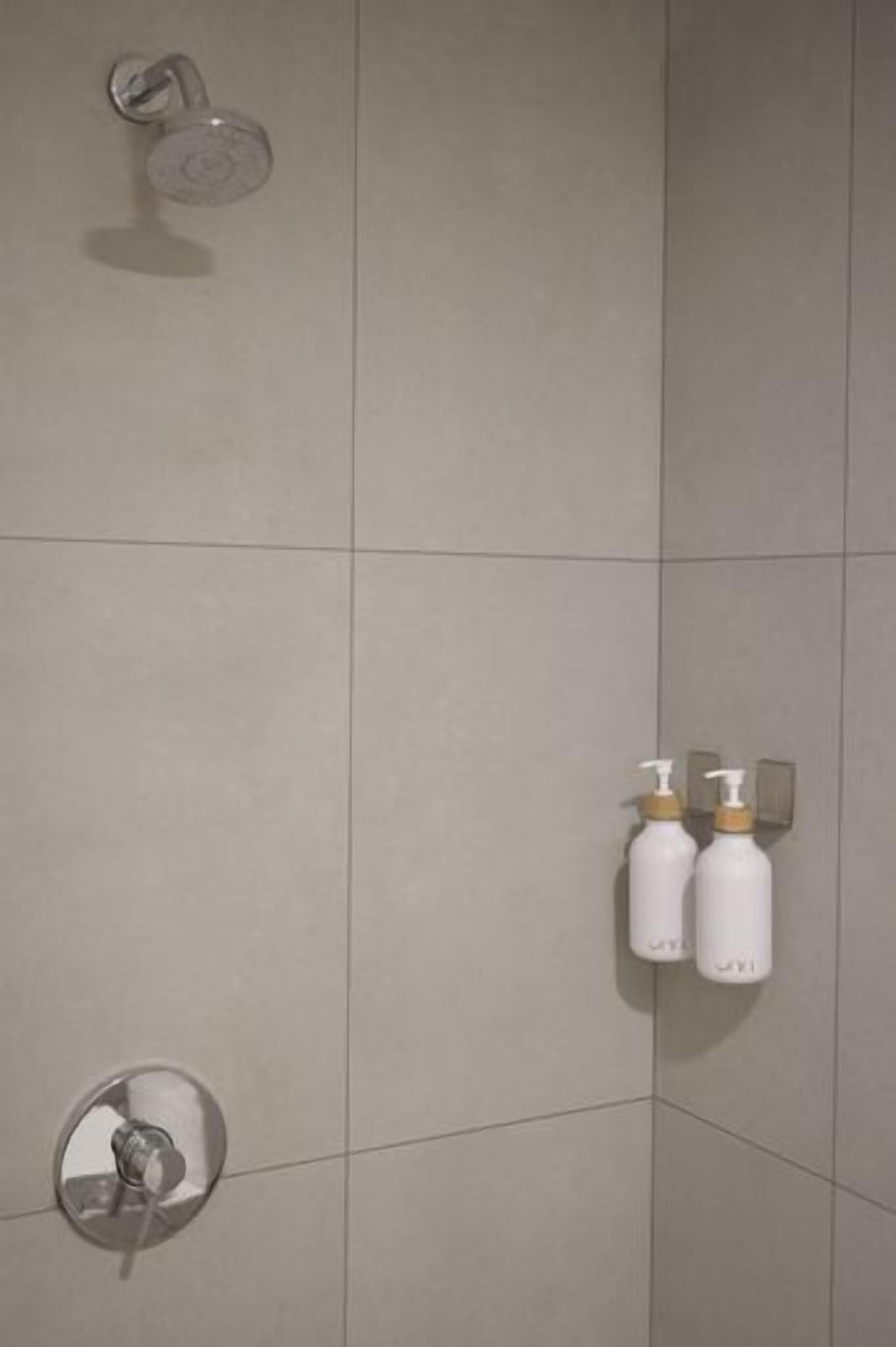 A tiled shower wall with two bottles of shampoo and conditioner.