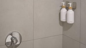 Paredes de azulejos no chuveiro, com duas garrafas de shampoo e condicionador.