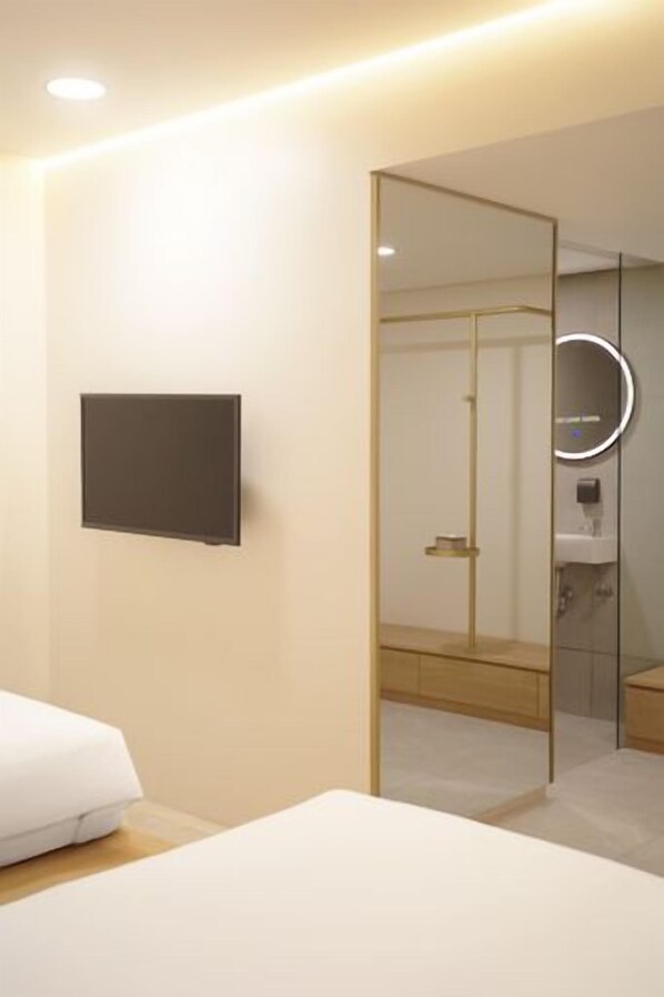Ein modernes Hotelzimmer mit einem Bett, einem Flachbildfernseher, einem Spiegel und einem durch eine Glaswand abgetrennten Badezimmer.