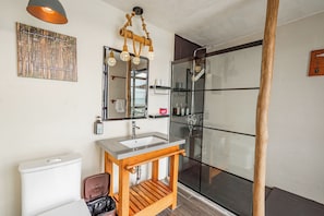 Un baño con tocador de madera, cabina de ducha con mampara de cristal y un cuadro en la pared.
