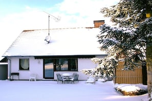 Ein Haus mit Satellitenschüssel, einer überdachten Terrasse mit Stühlen und einem mit Schnee bedeckten Rasen.