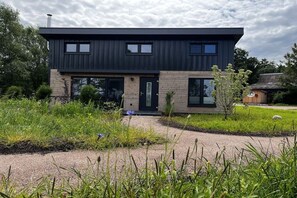 A modern two-story house with a dark exterior, a front door, and a small garden area with grass and a tree. - Holiday home in Wanna with Wi-Fi and parking (Wanna)