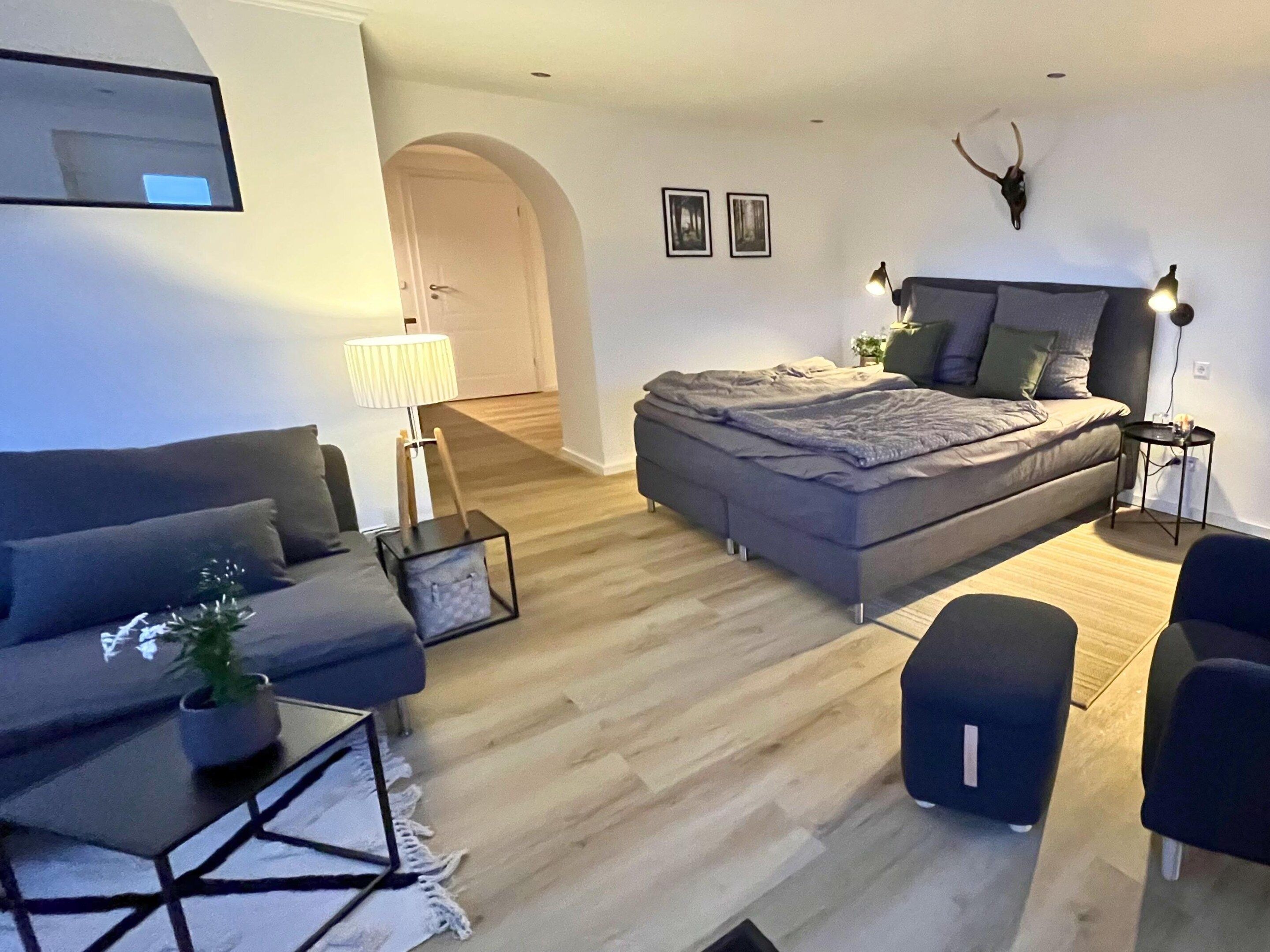 A modern living room with a sofa, a bed, a small table, and a lamp.