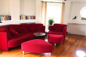 A living room with a red sofa, matching ottoman, and armchairs, a small round table, and a bookshelf with books. - Holiday home in Cuxhaven with swimming pool (Cuxhaven)