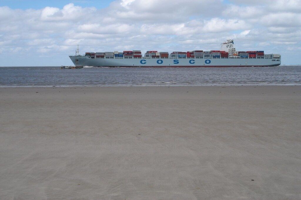 Ein großes Frachtschiff mit dem Namen 'COSCO' an der Seite, das auf dem Ozean fährt.