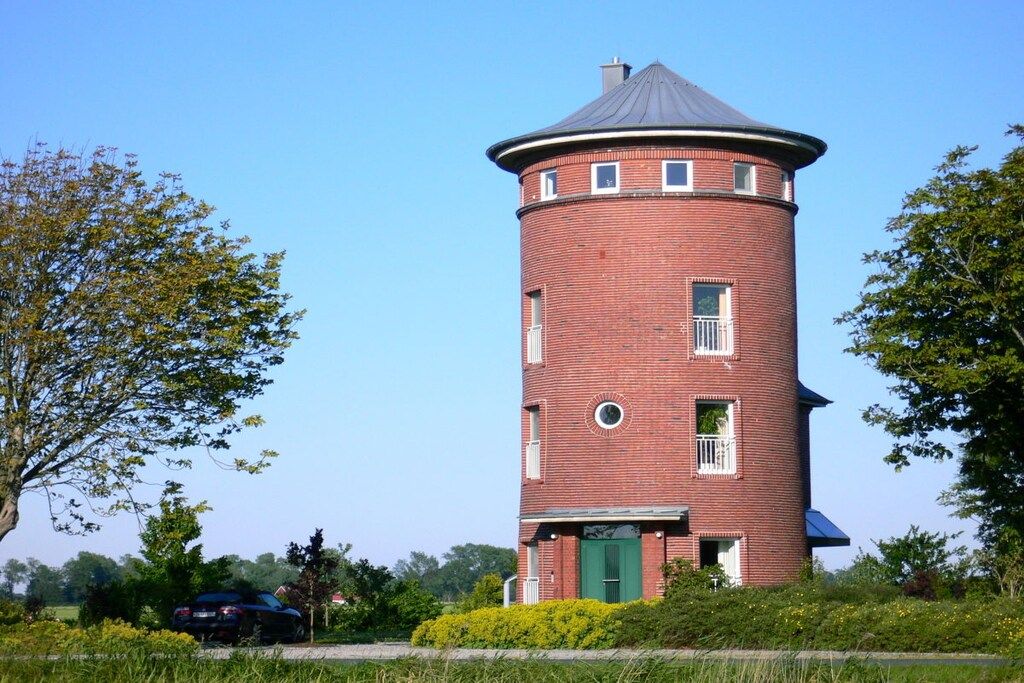A brick tower with a green door, surrounded by greenery and a clear sky.