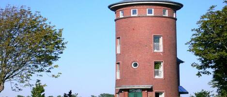 A brick tower with a green door, surrounded by greenery and a clear sky.