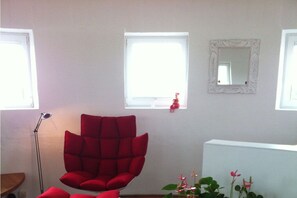 A room with a red chair, a floor lamp, a window, and a mirror on the wall. - Holiday home in Cuxhaven with swimming pool (Cuxhaven)