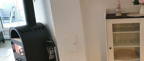 Une pièce avec un poêle en bois noir, un meuble blanc aux portes vitrées et une petite table sur laquelle se trouvent un vase et des livres.