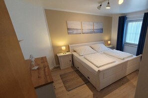 A bedroom with a bed, bedside tables, a nightstand, a wall-mounted artwork, and a window with curtains. - Holiday apartment with 2 bedrooms (Wenkendorf)