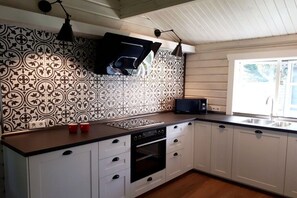 A kitchen with white cabinets, a black oven, a microwave, and a window with a view of greenery. - Time out The holiday home (Müden\/Örtze)