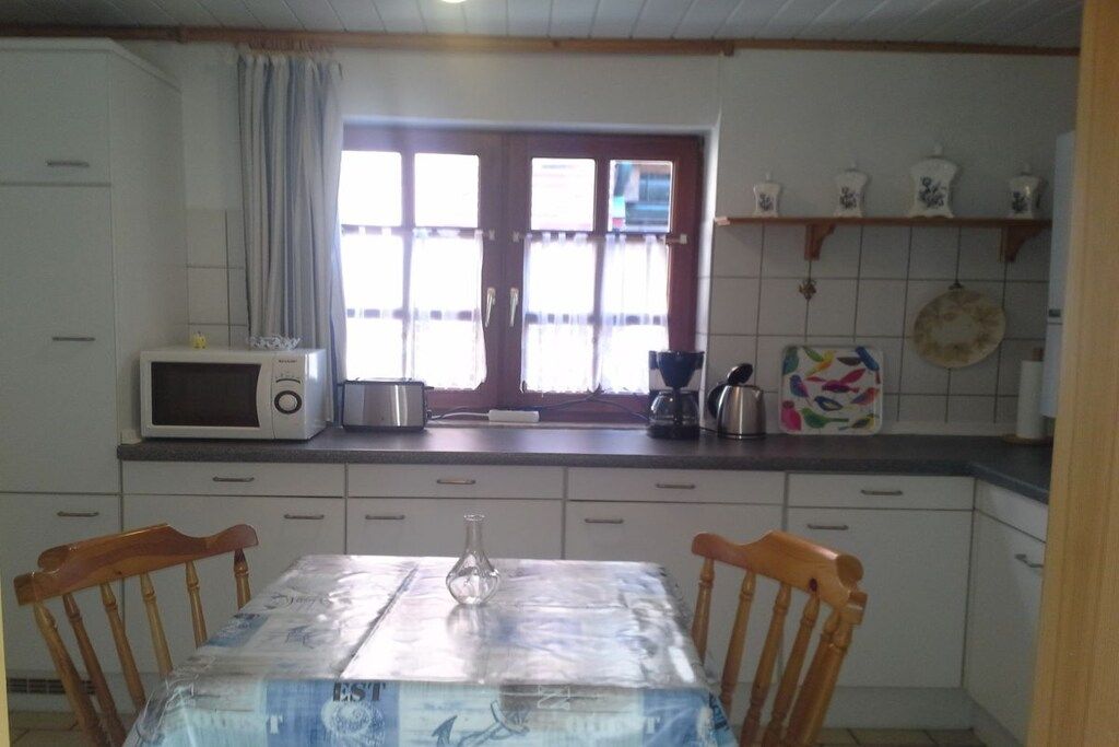 A kitchen with white cabinets, a microwave, a coffee maker, and a window with curtains.
