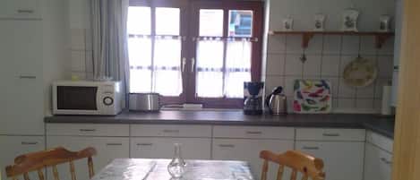 A kitchen with white cabinets, a microwave, a coffee maker, and a window with curtains.