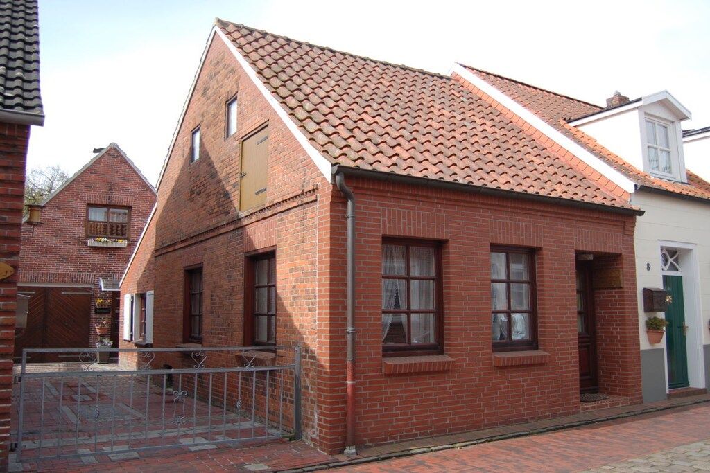 A red brick building with a tiled roof, a gated entrance, and a small porch area.