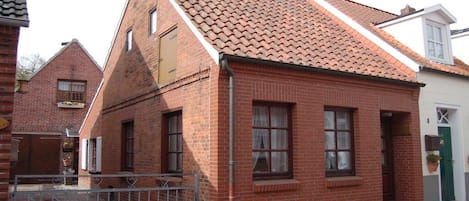 A red brick building with a tiled roof, a gated entrance, and a small porch area.