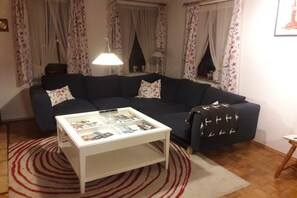 A living room with a dark blue sofa, a white coffee table with magazines, a patterned throw blanket, and a red and white rug. - Lüttje Huus an d" Kark (Krummhörn)