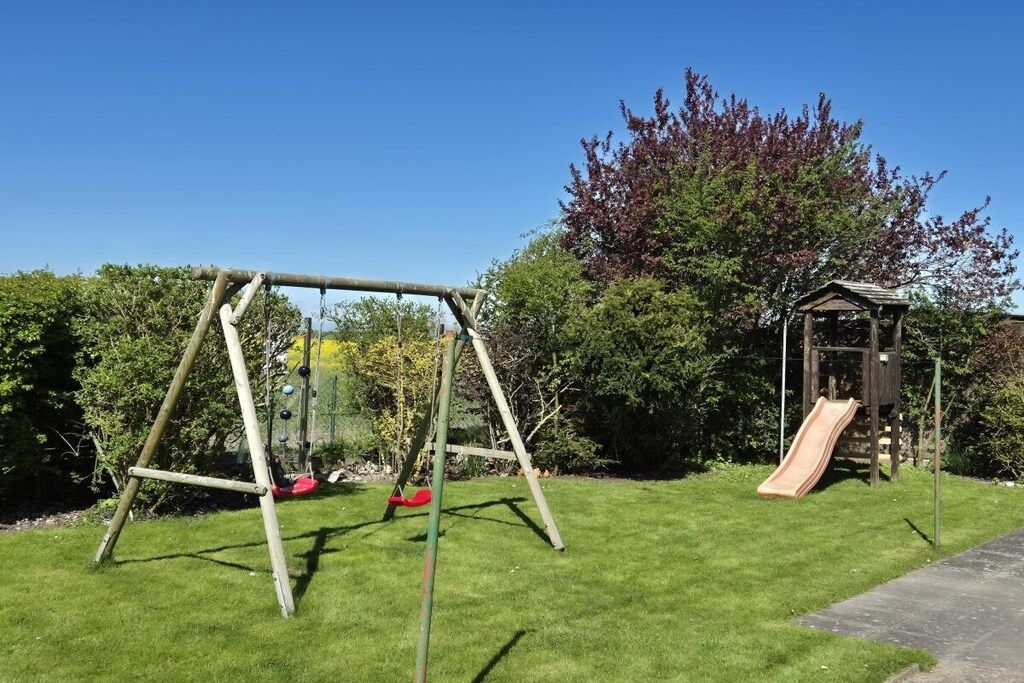 A playground with a swing set and a slide, surrounded by a well-maintained lawn and trees.