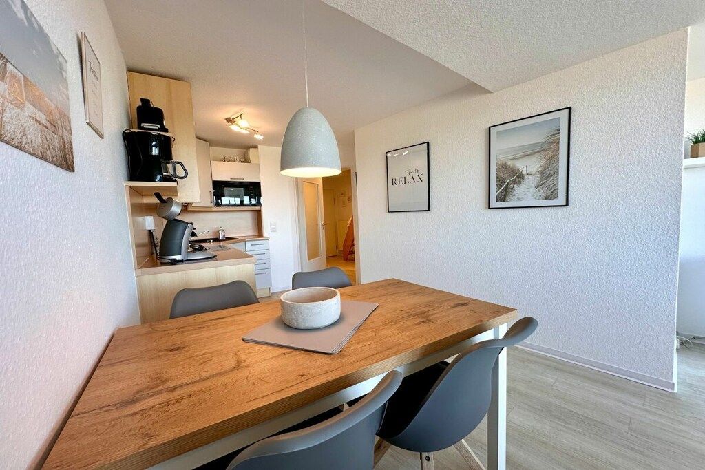 Una cocina moderna con cafetera, tetera y comedor con mesa y sillas de madera.